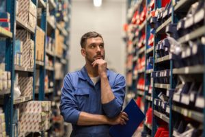 man in a factory holding a clip board and scratching his chin