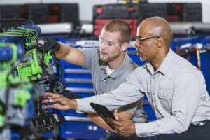An African American man instructing a Caucasian student on how to repair a diesel engine. He is teaching a class in a vocational school.
