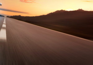 An image of a blurry road and a sunset over the hill.